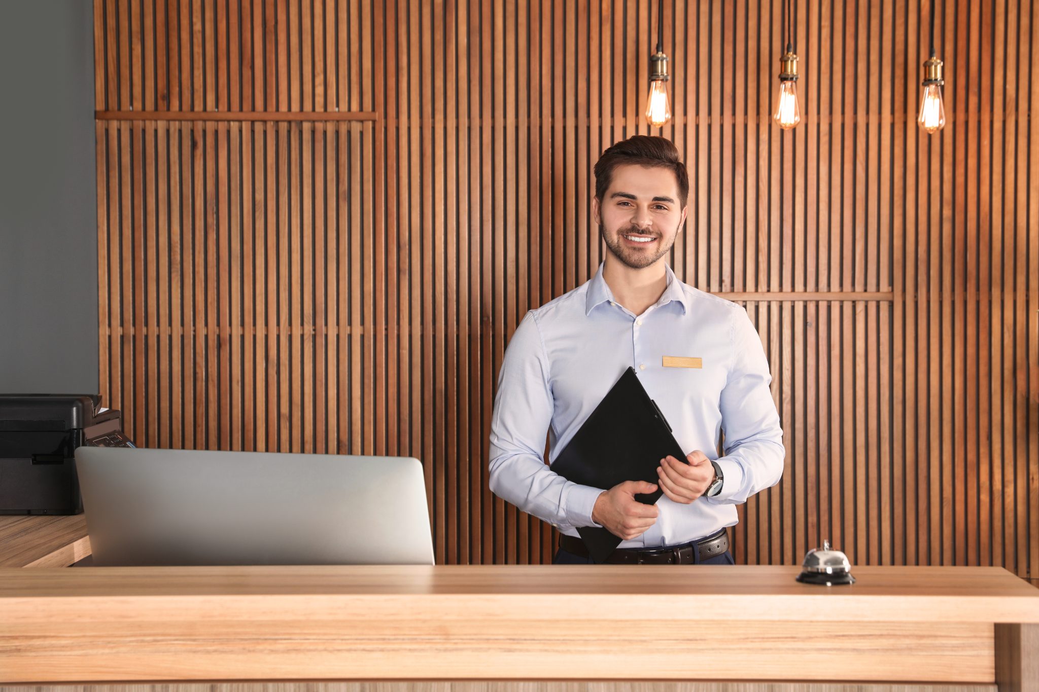 Smiling young hotel receptionist in a business shirt standing behind a front desk